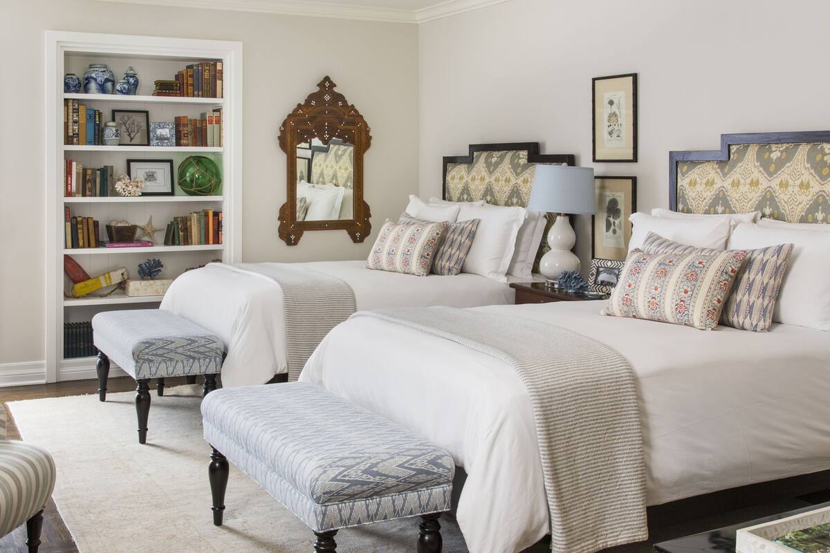 A bedroom with two beds, a bookshelf, and a mirror.