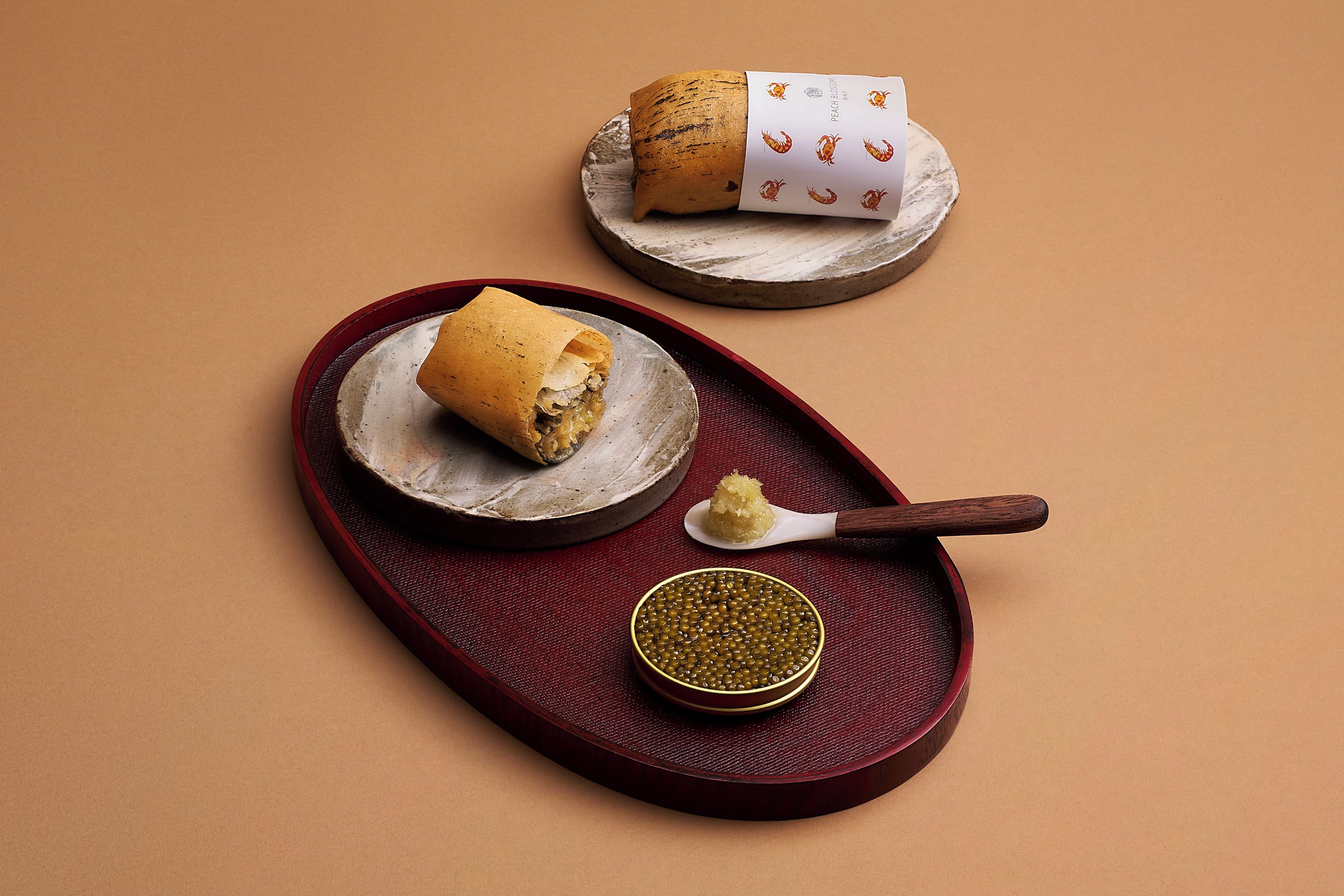 A food presentation with a rolled item on a plate, a spoon with a condiment, and a small bowl of a yellowish substance.