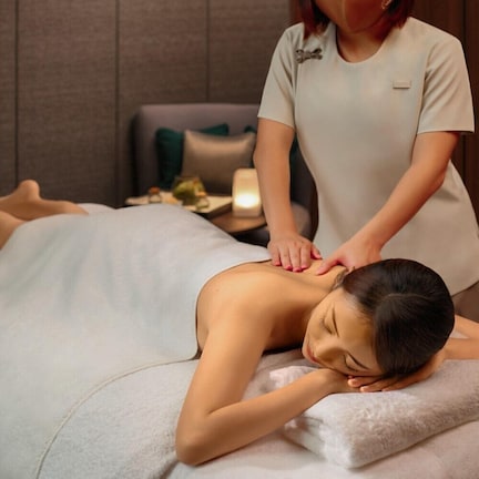 A person receiving a massage in a room with a bed, a nightstand, and a lamp.
