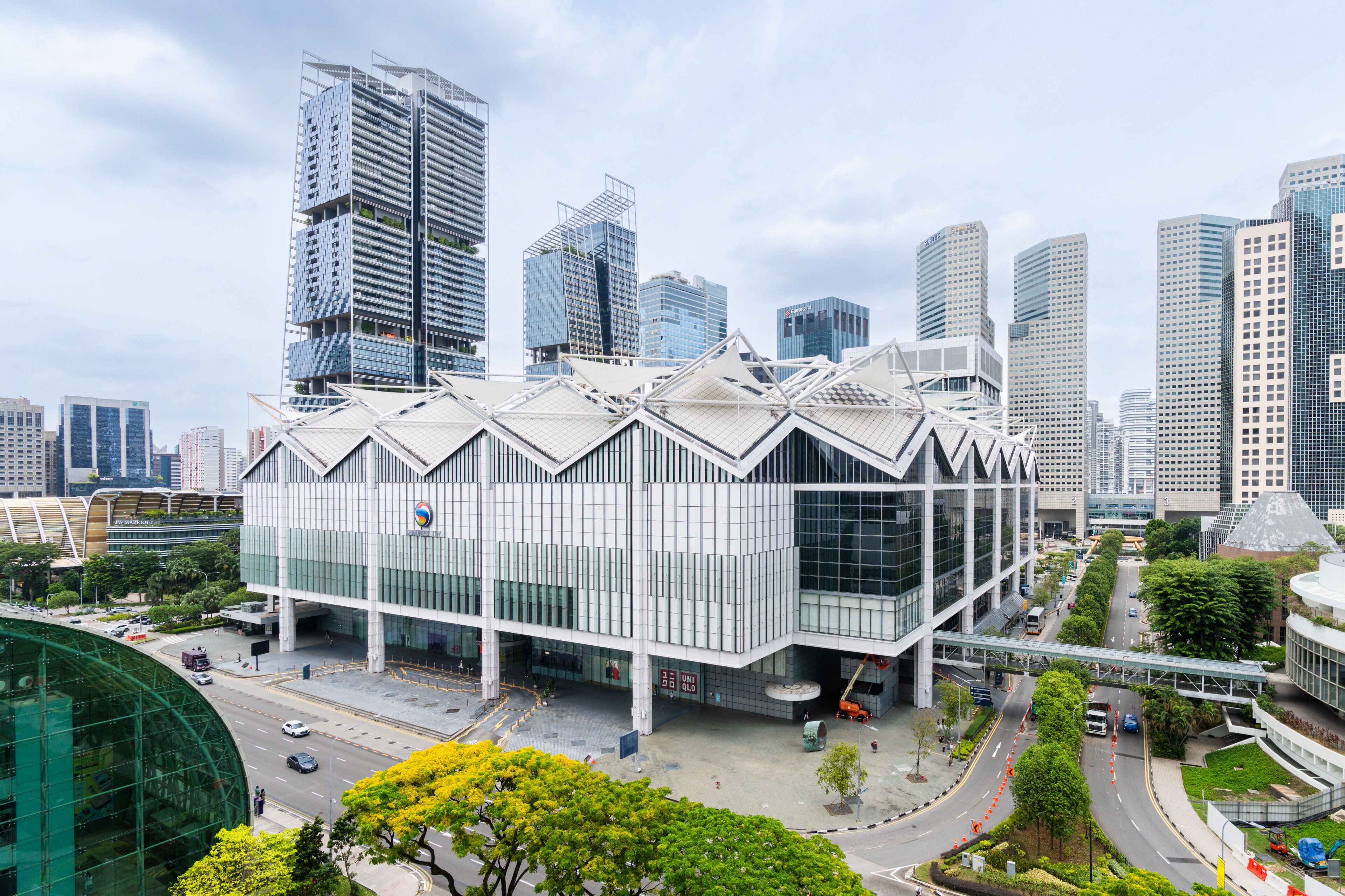 A modern building with a unique geometric roof design, surrounded by high-rise buildings.
