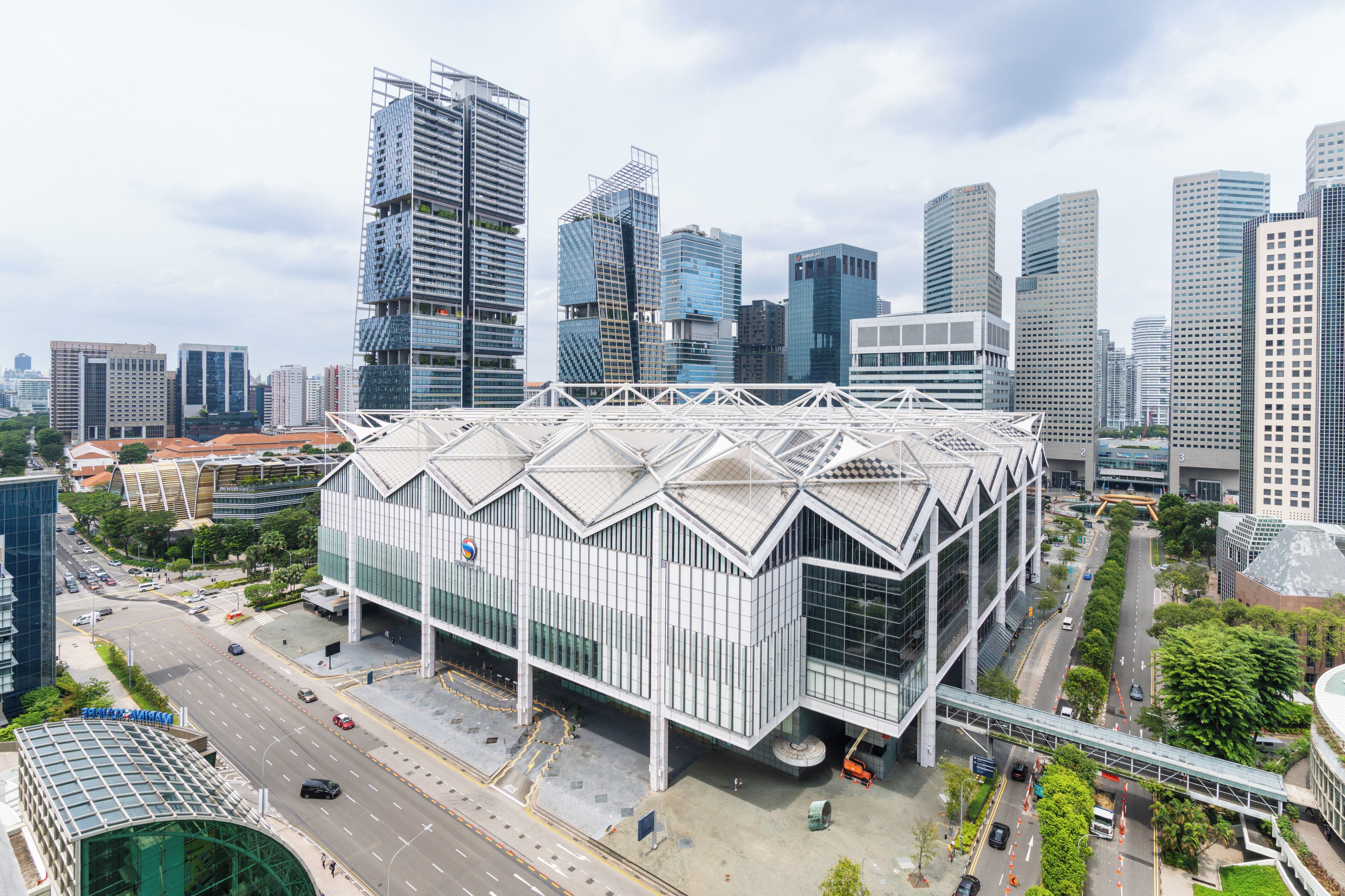 A modern building with a unique geometric roof structure, surrounded by a cityscape with high-rise buildings.