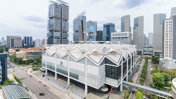 A modern building with a unique geometric roof structure, surrounded by a cityscape with high-rise buildings.
