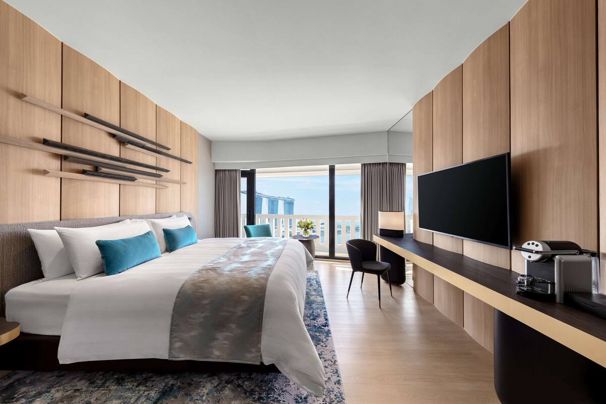 Ein modernes Hotelzimmer mit einem großen Bett, einem Flachbildfernseher, einem Schreibtisch mit Kaffeemaschine und Blick auf die Stadt.