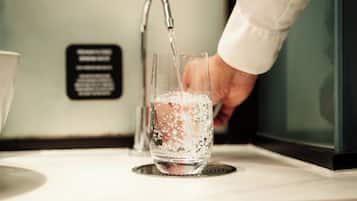 Una mano vertiendo agua en un vaso con burbujas, un grifo y un cartel con texto.