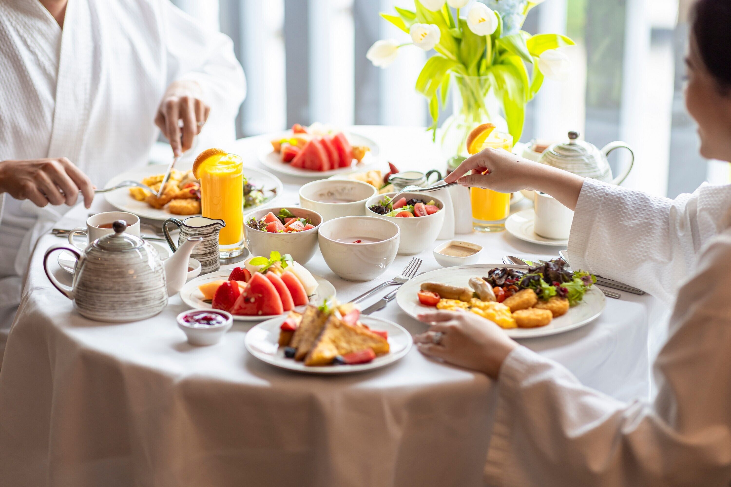 A breakfast table with various dishes, a pitcher, and a vase with flowers.