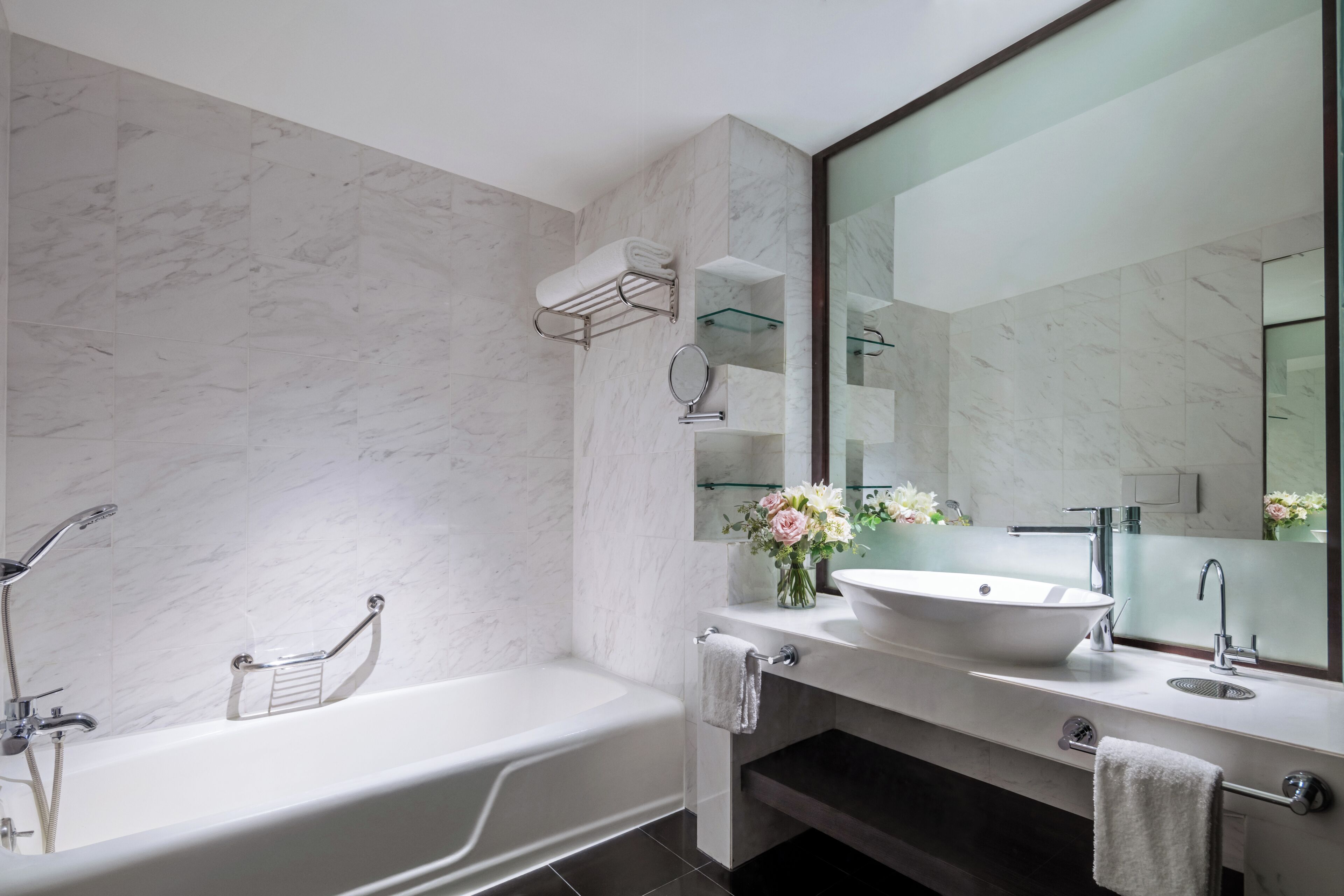 A modern bathroom with a freestanding bathtub, a large mirror, and a vanity with a sink and towel rack.