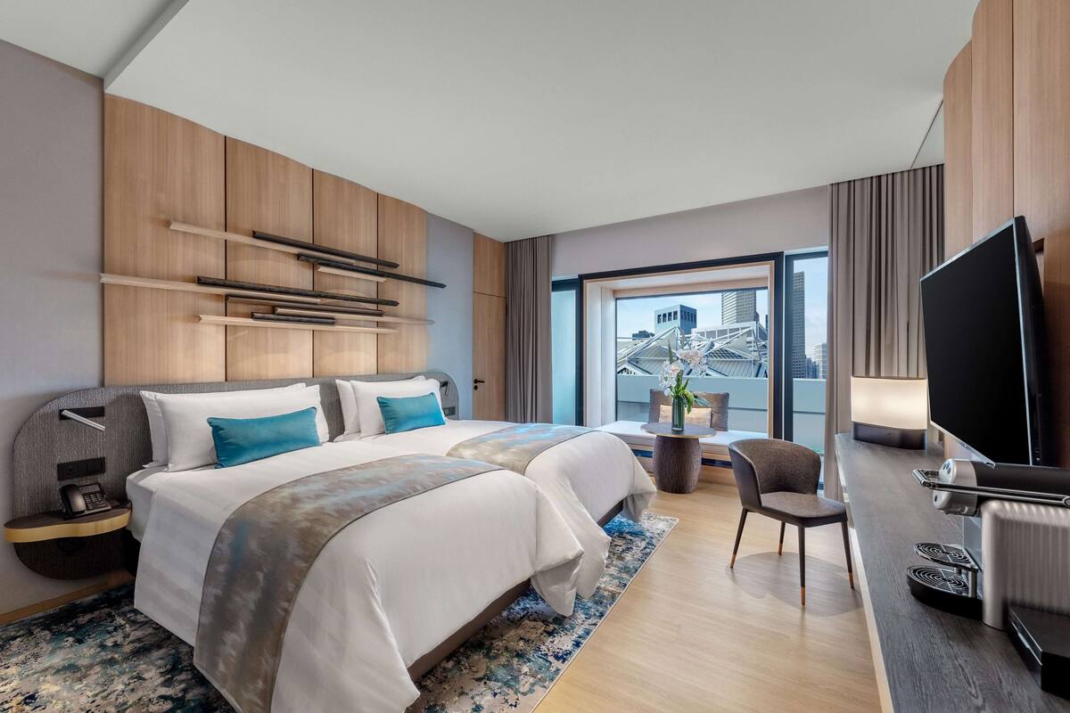 Ein modernes Hotelzimmer mit einem großen Bett, einem Schreibtisch, einem Flachbildfernseher und Blick auf die Stadt durch das Fenster.