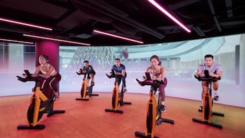 A group of people on stationary bikes in a gym with a modern design and a large screen in the background.