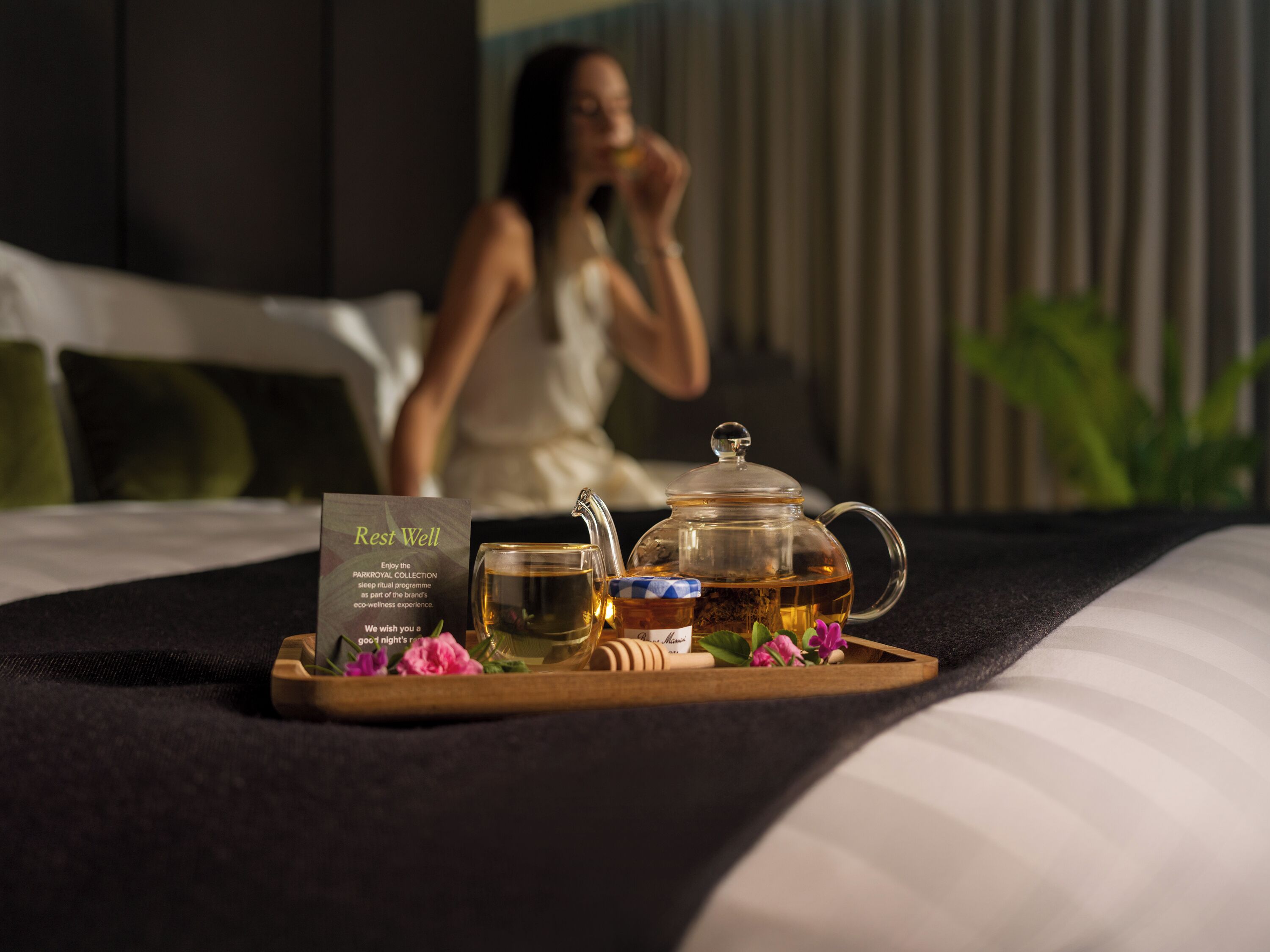 A tray with a teapot, a glass, and a sign on a bed.