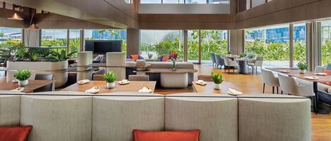 Un salón moderno y abierto con disposición de asientos, una zona de comedor y amplios ventanales con vistas a la ciudad.