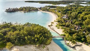 Vista aérea de un complejo turístico frente al mar, con playa, aguas turquesas cristalinas y exuberante vegetación.