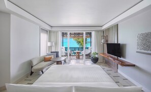 Habitación de hotel con cama, zona de estar con mesa y sillas, televisor y vista al océano.