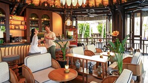Un restaurante con mobiliario de madera, techo de paja y una zona de bar.