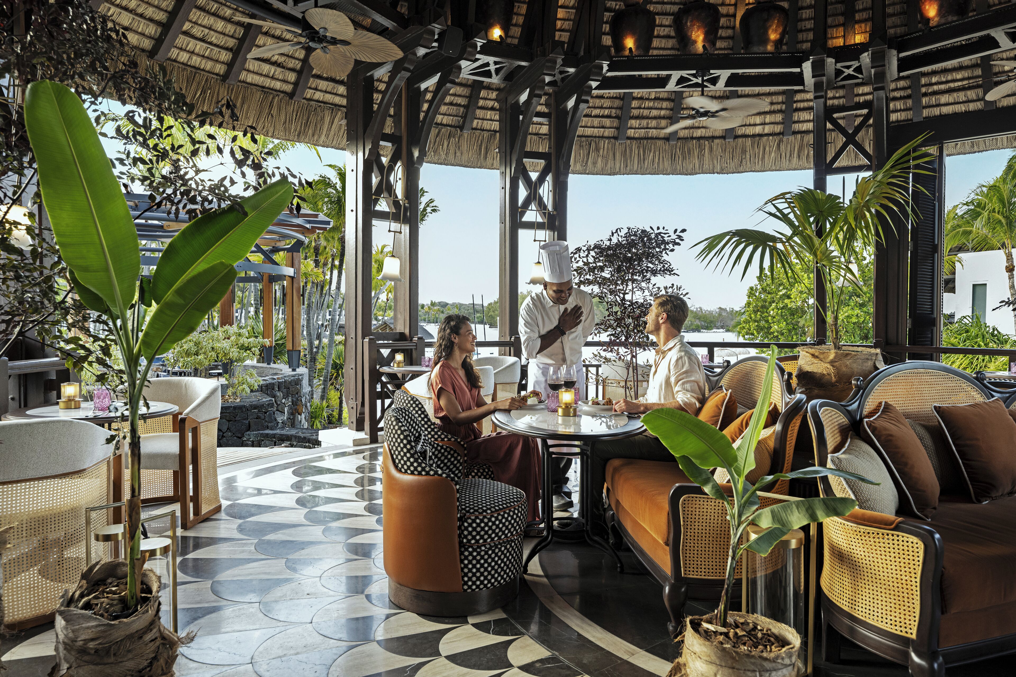 An outdoor seating area with round tables, wicker furniture, and potted plants.