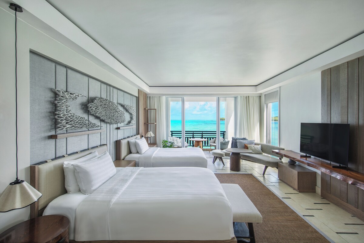 Ein Hotelzimmer mit zwei Betten, einem Fernseher, einem Balkon mit Meerblick und einer Essecke.