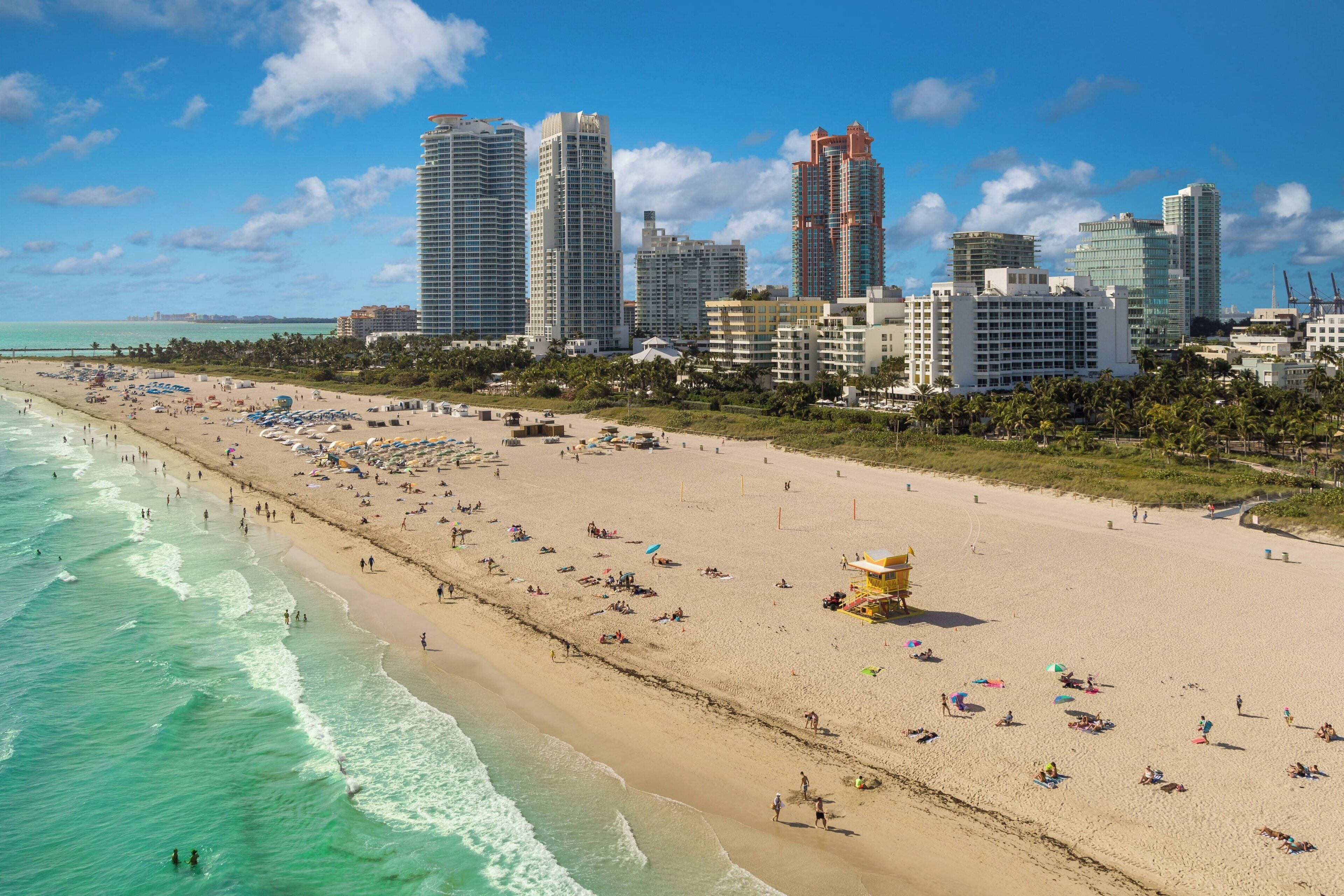 Una playa con una torre de salvavidas, una orilla arenosa y un horizonte urbano con edificios altos.
