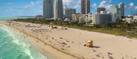 Una playa con una torre de salvavidas, una orilla arenosa y un horizonte urbano con edificios altos.