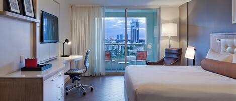 Habitación de hotel con cama, escritorio, silla y un amplio ventanal con vista a la ciudad.