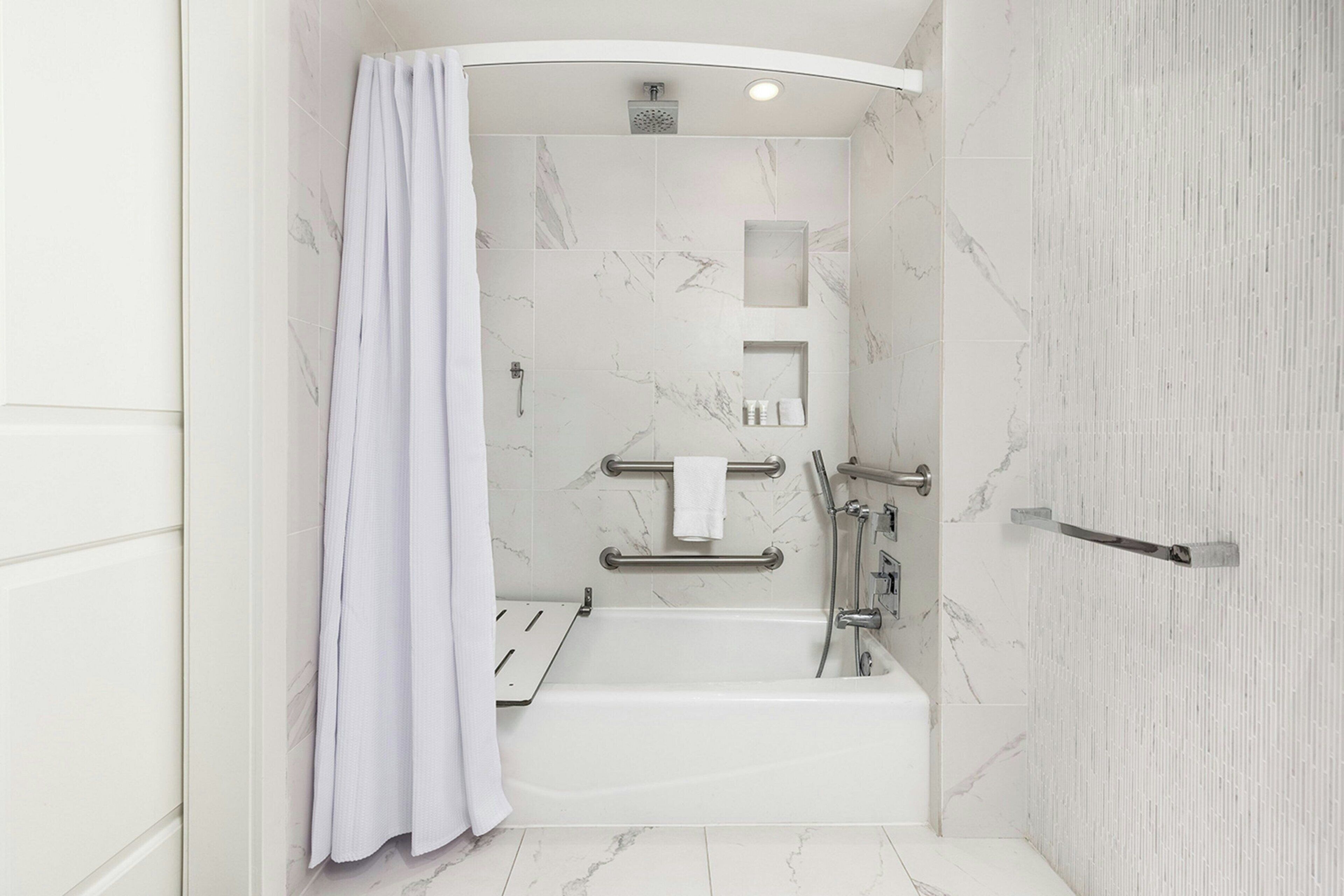 A modern bathroom with a bathtub, shower, and grab bars.