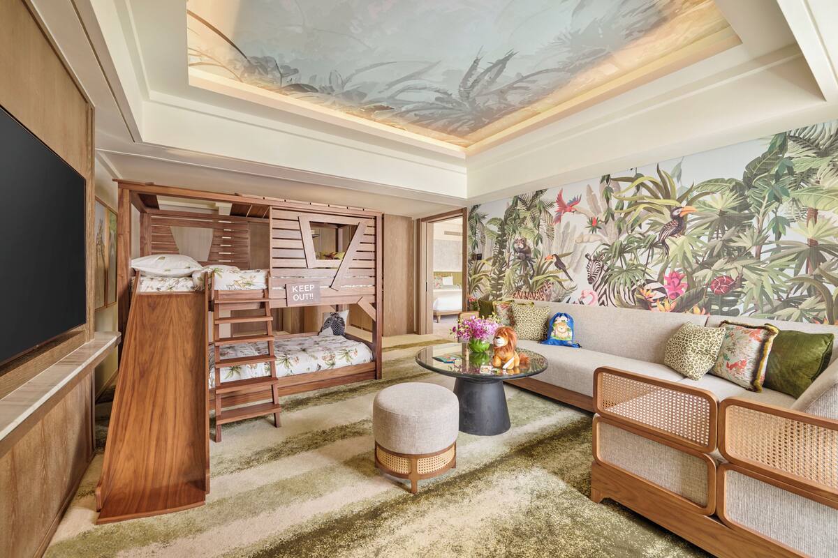 Un salón moderno con un televisor de pantalla plana grande, un sofá, una mesa de centro y un mural de follaje tropical.