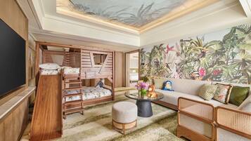 Ein modernes Wohnzimmer mit einem großen Flachbildfernseher, einem hölzernen Bett mit zahlreichen Stauraumfächern, einer Couch und einem tropischen Wandbild.