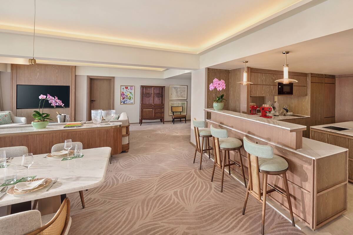 Een moderne keuken met houten kastjes, een centraal eiland, barkrukken en een eethoek met een tafel voor vier personen.