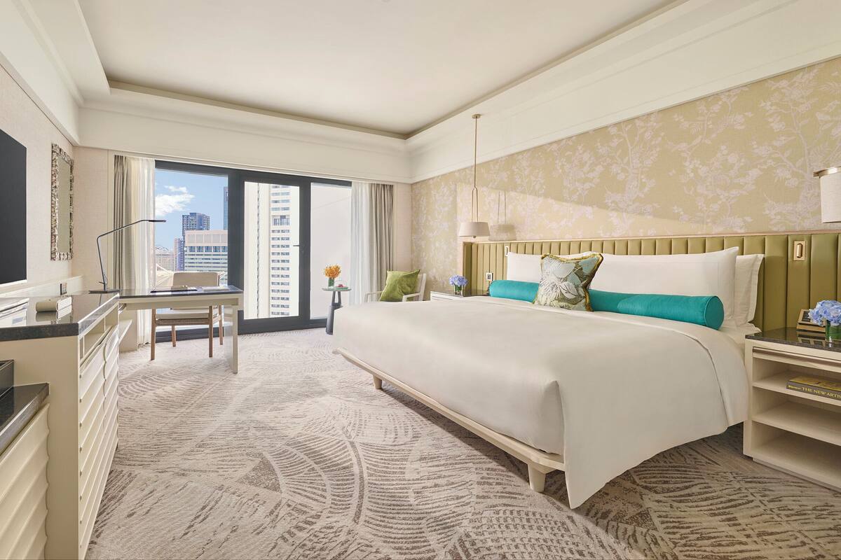 Habitación de hotel con una cama grande, un escritorio con silla, televisión y vista a la ciudad desde la ventana.