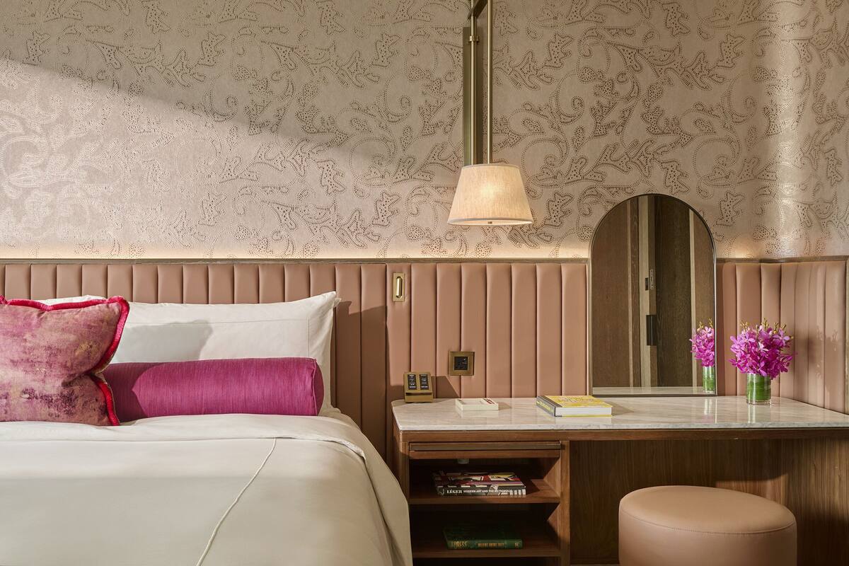 Een hotelkamer met een bed, nachtkastje, spiegel en een bureau met lamp.