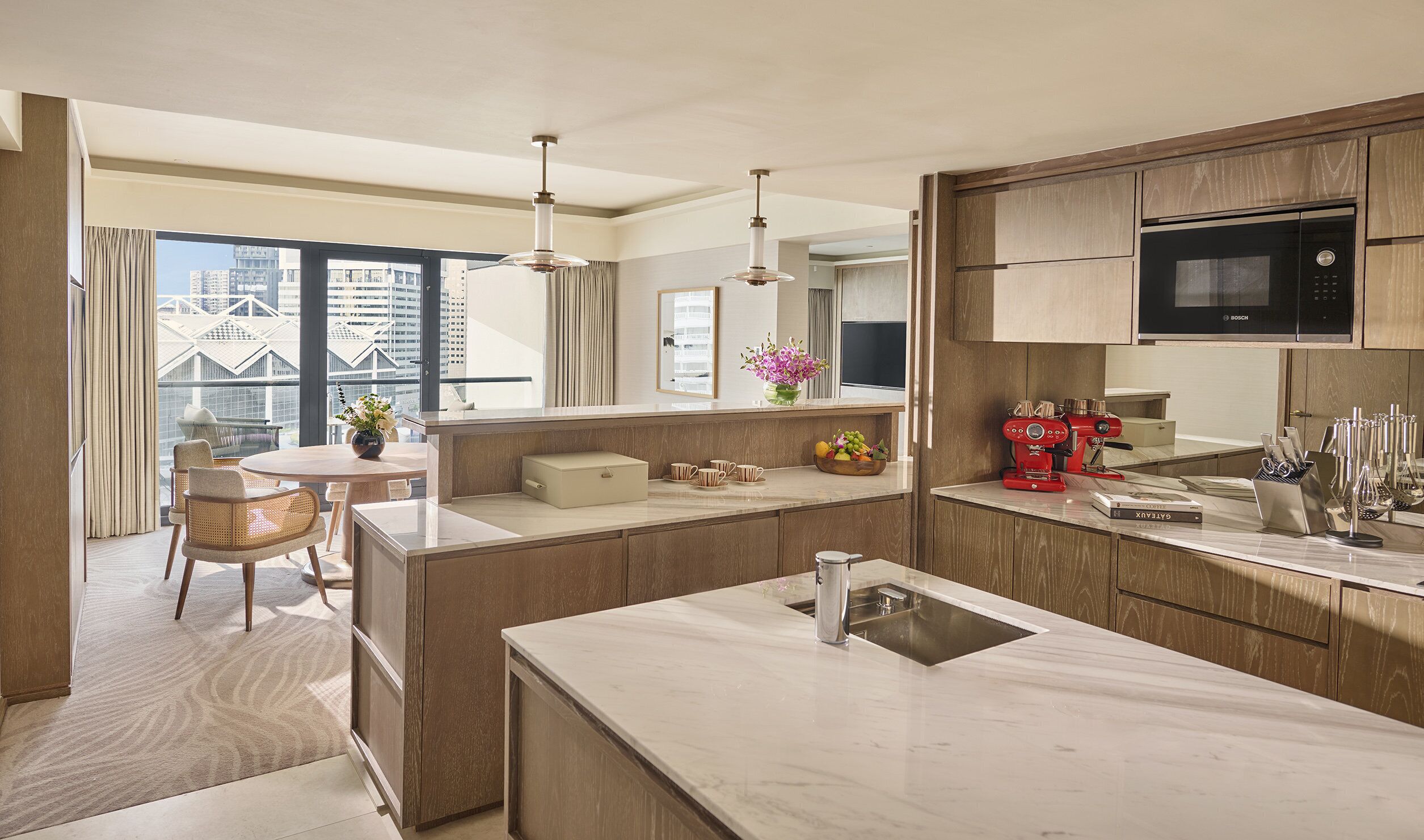 A modern kitchen with a central island, a dining area with a table and chairs, and a large window offering a city view.