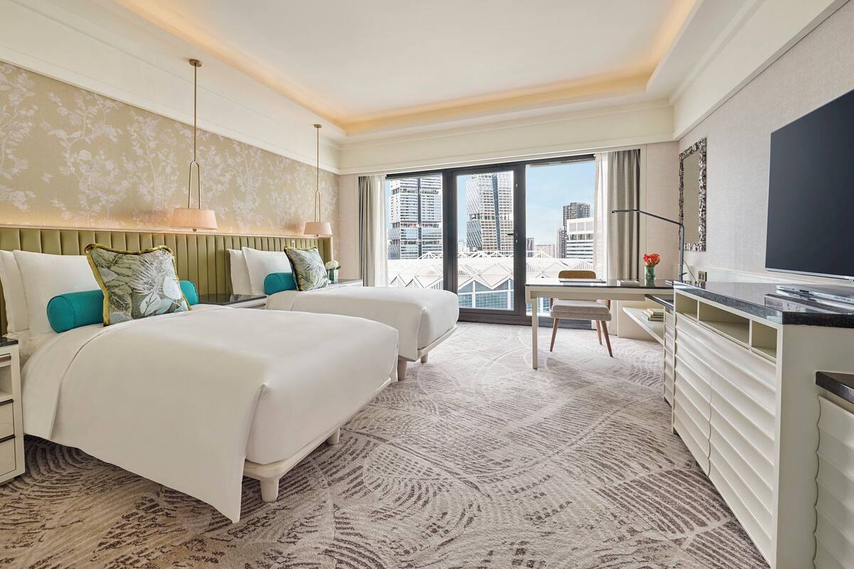 Een hotelkamer met twee bedden, een bureau, een televisie en uitzicht op de stad.