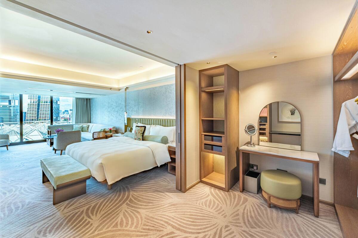 Een moderne hotelkamer met een groot bed, een bureau met spiegel, een zithoek en uitzicht op de stad.