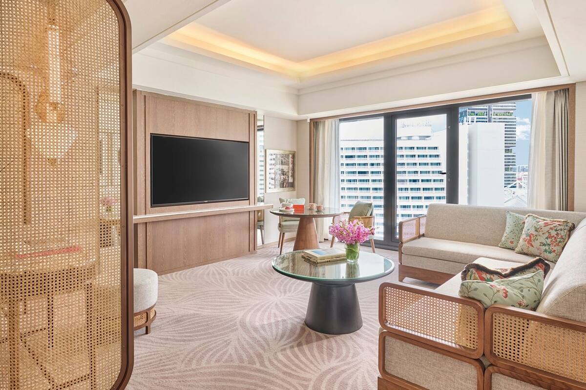 Een moderne hotelkamer met een grote televisie, comfortabele zithoek, een glazen bijzettafeltje en uitzicht op de skyline.