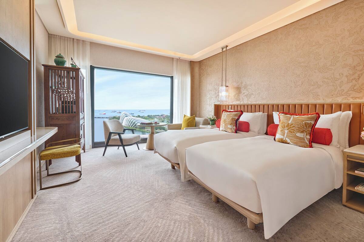 Een hotelkamer met twee bedden, een televisie, een bureau en uitzicht op zee.