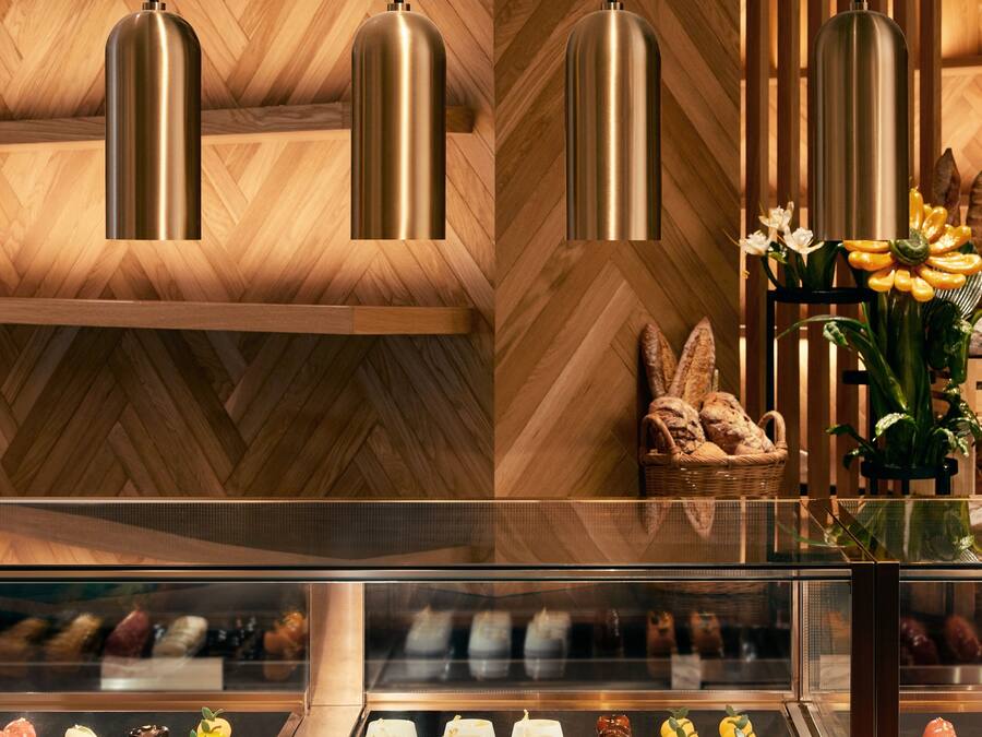 Mostrador de panadería con diversos pasteles y un interior de madera con luces colgantes.