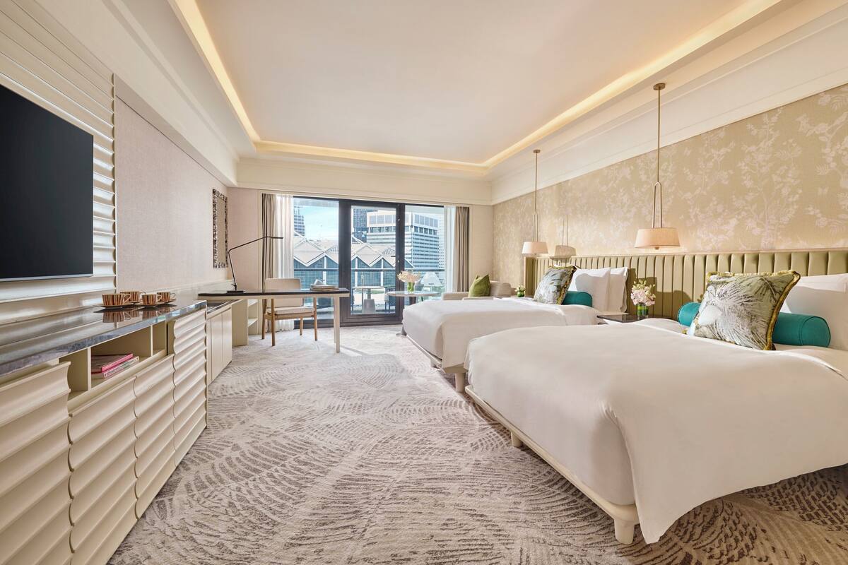 Een hotelkamer met twee bedden, een bureau, een televisie en uitzicht op de stad.