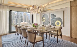 A dining area with a city view, modern chandelier, abstract wall art, and a patterned rug.