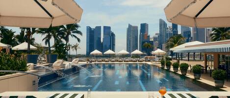 A rooftop pool with lounge chairs and umbrellas, overlooking a city skyline.