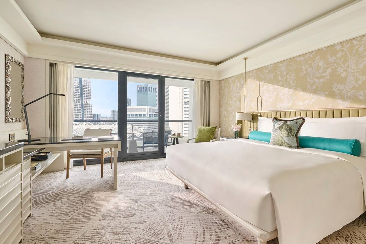 Een hotelkamer met een groot bed, een bureau en een stoel. Er is uitzicht op gebouwen buiten het raam.