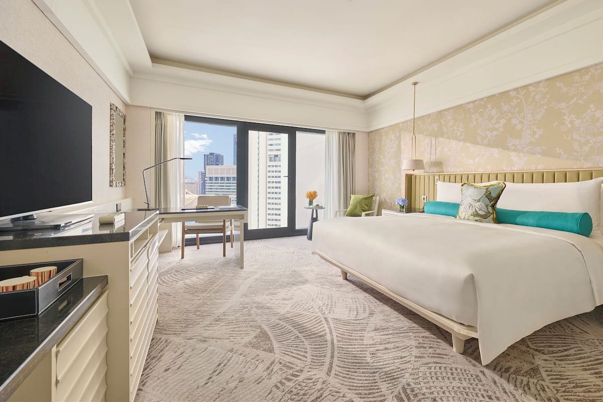 Een hotelkamer met een groot bed, een bureau met een stoel, een televisie en uitzicht op de stad.