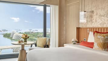 Habitación de hotel con un ventanal que ofrece vistas a la costa, una cama, una mesita de noche y una pequeña mesa con flores.