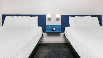 Habitación de hotel con dos camas, un cabecero azul, dos lámparas de noche y una mesita con un teléfono.