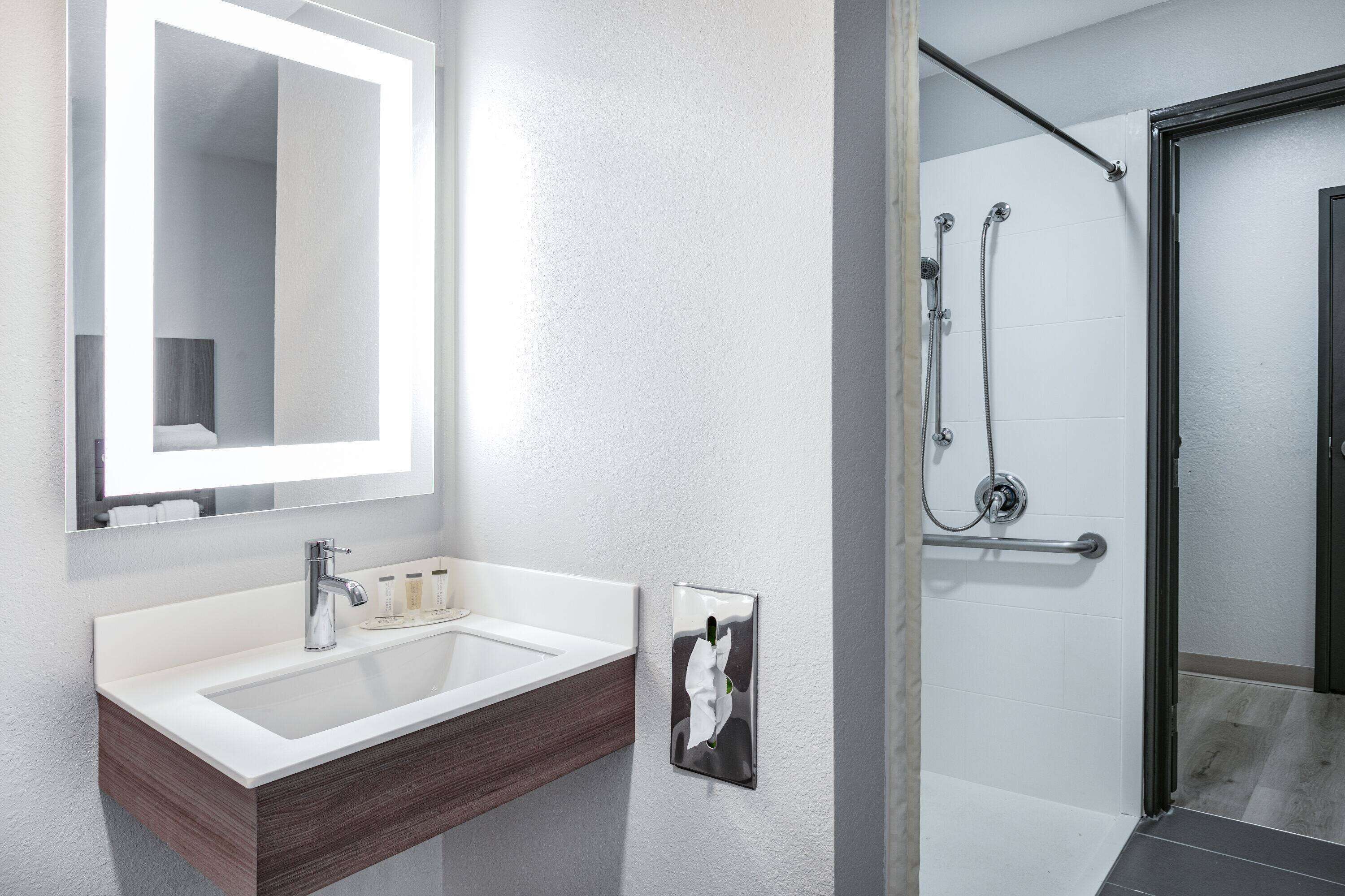 A modern bathroom with a white sink, a mirror, and a shower area.