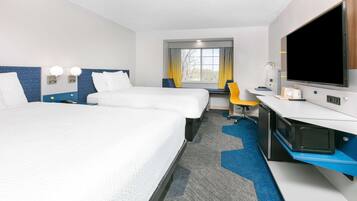 A hotel room with two beds, a desk, a television, and a window with curtains.