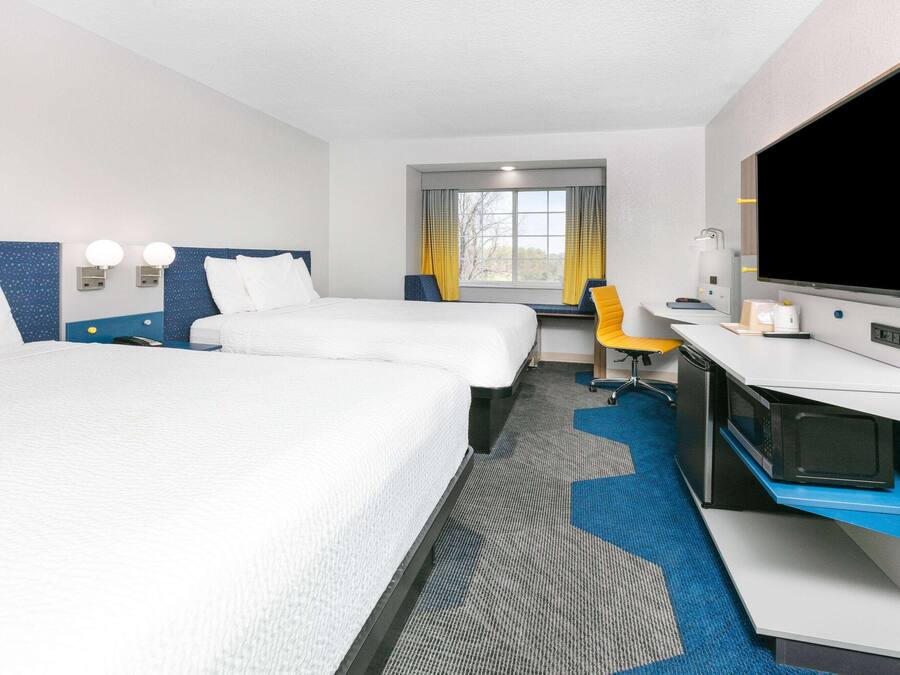 A hotel room with two beds, a desk, a television, and a window with curtains.