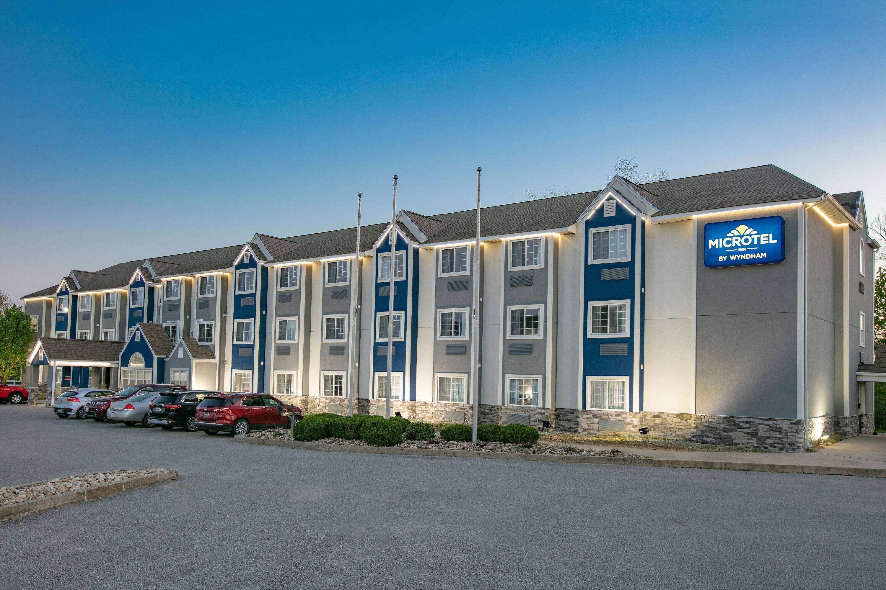 Um hotel Microtel by Wyndham com uma fileira de edifícios térreos, estacionamento e céu limpo.
