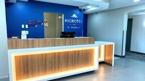A reception desk at a Microtel Inn with a blue wall and a sign indicating check-in and check-out times. - Microtel Inn by Wyndham Beckley (Beckley)
