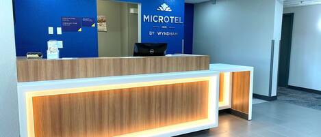 Un comptoir d’accueil dans un hôtel Microtel Inn, avec un mur bleu et un panneau indiquant les heures d’arrivée et de départ.