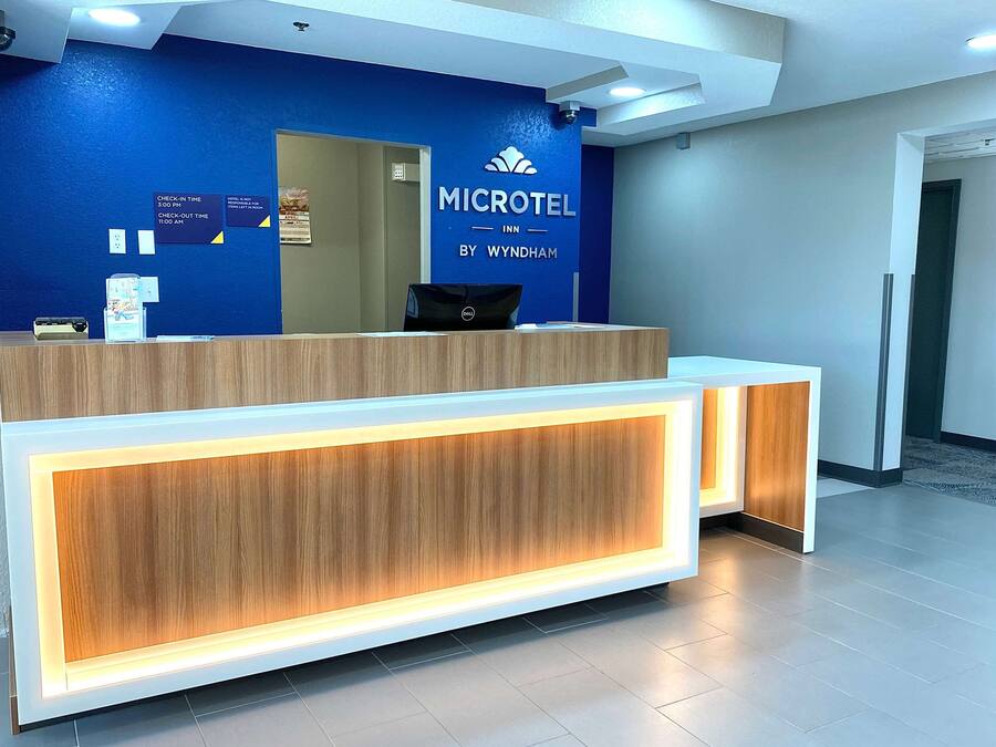 Un mostrador de recepción en un Microtel Inn, con una pared azul y un letrero que indica los horarios de registro de entrada y salida.