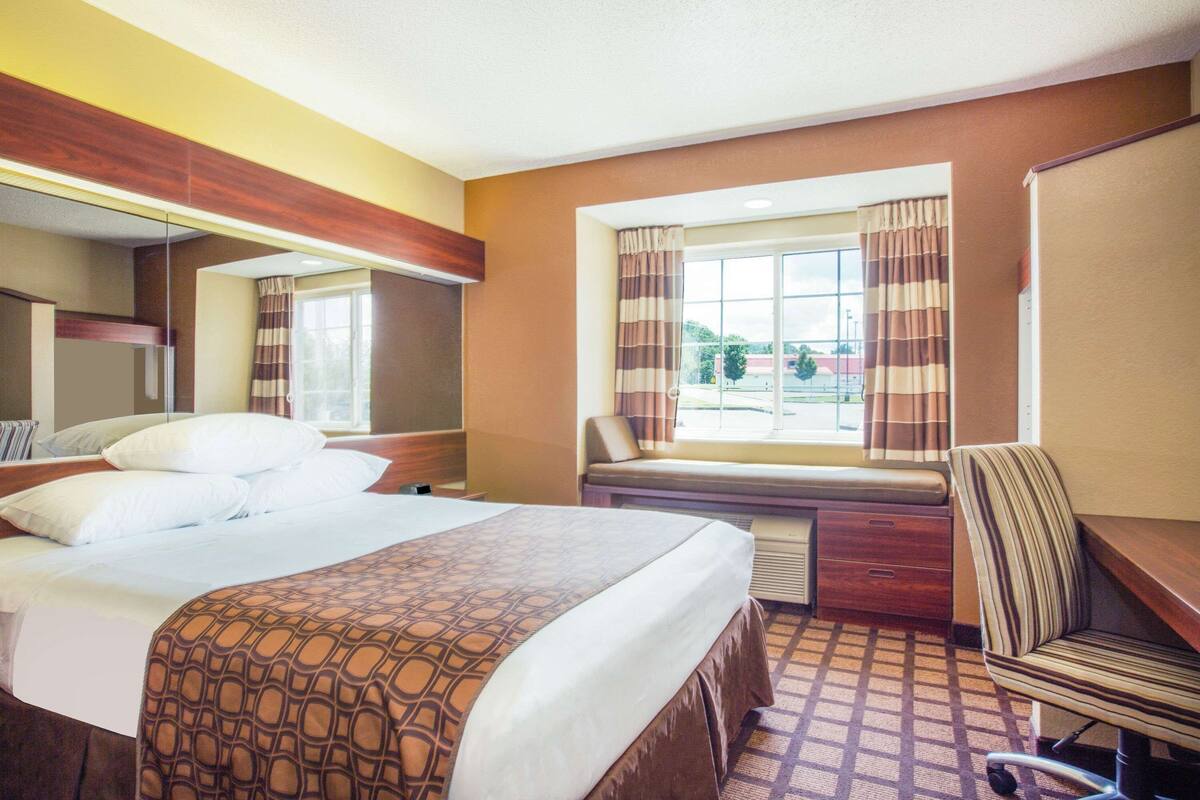 Ein Hotelzimmer mit Bett, Schreibtisch, Stuhl, einem Fenster mit Vorhängen und Blick nach draußen.
