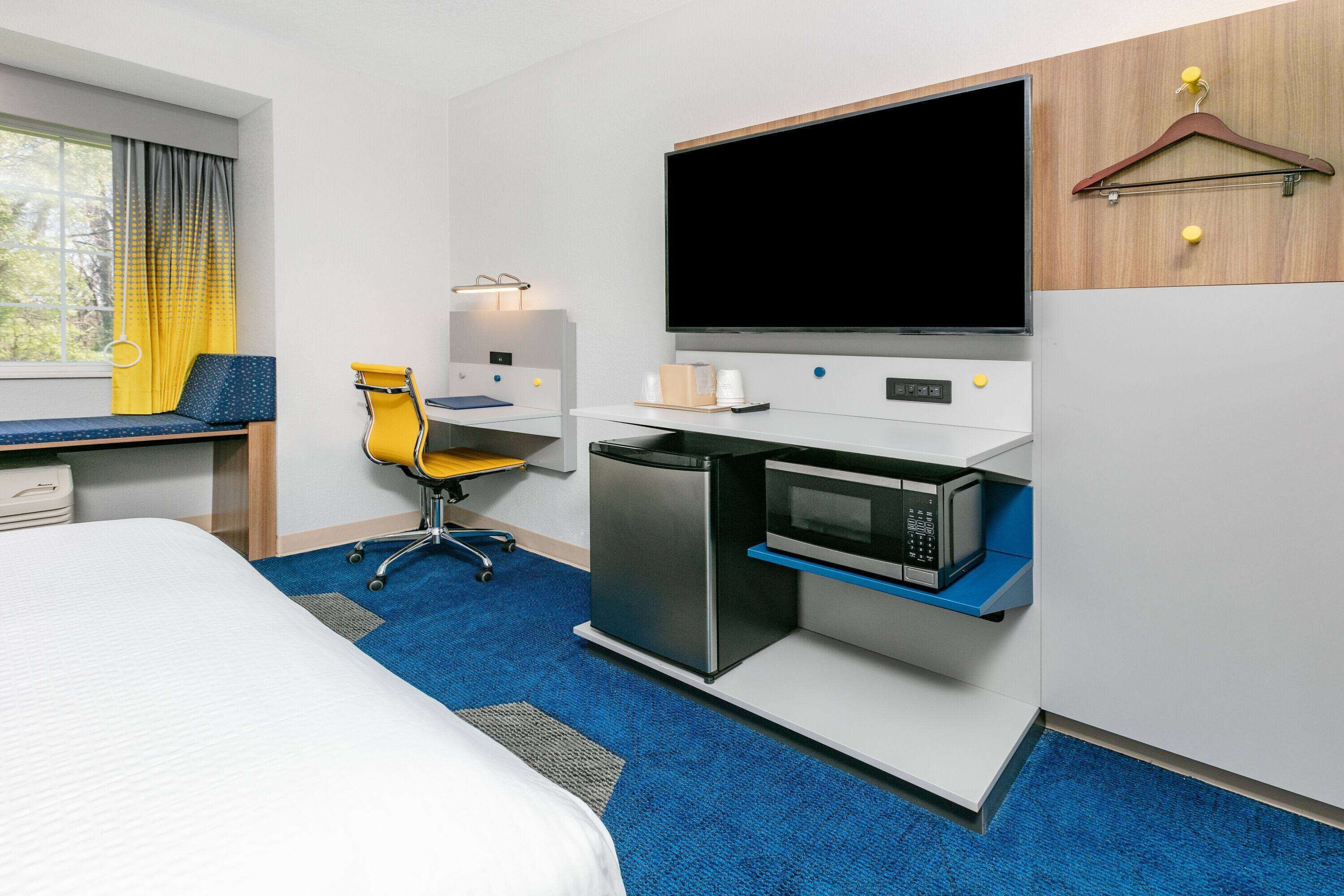 A hotel room with a bed, a desk with a computer, a microwave, and a TV.